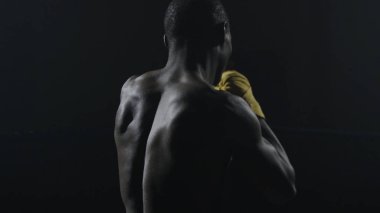 Kaslı adam siyah arka plan üzerine boks dikiz. Gölge boks pratik Afro Amerikan genç erkek boxer. Sarı boks eldivenleri boksör