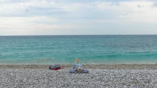 Blick von oben auf junge schöne Frau, die sich am Kiesstrand im schönen Meer entspannen. Filmmaterial. Frau liegt auf Kieselsteinen am Strand — Stockvideo