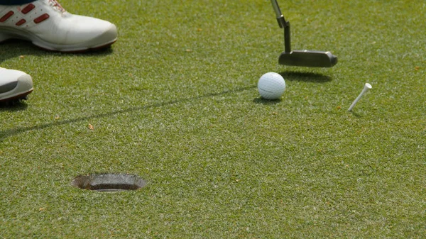 Profesyonel golfçü topu deliğe sokuyor. Güneşli bir günde arka planda oyuncuyla deliğin kenarında golf topu. — Stok fotoğraf