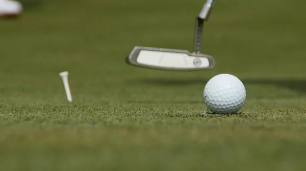 Profesyonel golfçü topu deliğe sokuyor. Güneşli bir günde arka planda oyuncuyla deliğin kenarında golf topu — Stok fotoğraf