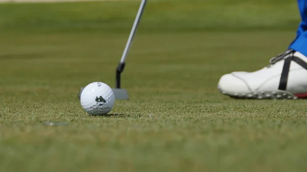 Golfprofi legt Ball ins Loch. Golfball am Lochrand mit Spieler im Hintergrund an einem sonnigen Tag — Stockfoto