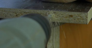 Adam bir tatbikat elinde tutar ve bir delik ahşap bir yönetim kurulu yapar. Ahşap talaşı etrafında uçan. Yakın çekim