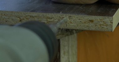 Adam bir tatbikat elinde tutar ve bir delik ahşap bir yönetim kurulu yapar. Ahşap talaşı etrafında uçan. Yakın çekim