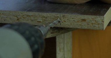 Adam bir tatbikat elinde tutar ve bir delik ahşap bir yönetim kurulu yapar. Ahşap talaşı etrafında uçan. Yakın çekim