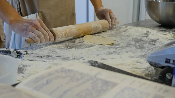 Detail of womans hand rolling out a dough with a rolling pin while making homemade pasta. Womans hands rolling dough — Stock Photo, Image