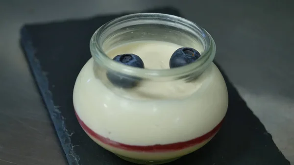 Iogurte caseiro com mirtilos em um frasco de vidro. Mão colocando morango em iogurte, close — Fotografia de Stock