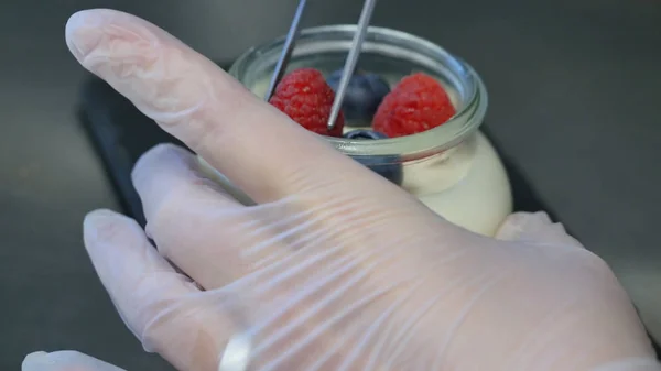 Iogurte caseiro com mirtilos em um frasco de vidro. Mão colocando morango em iogurte, close — Fotografia de Stock