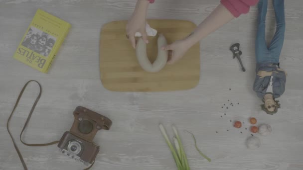 Les mains mettent la saucisse sur le tableau. Sur la table se trouve : un livre, un vieil appareil photo, un oignon, de l'ail et des images de jouets style instaram — Video