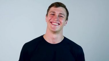 Mavi t-shirt genç İspanyol adamla portresi, ayakta ve gülüyor beyaz arka plan üzerinde - kahkaha kavramı izole. Adam giyen güçlü mavi t-shirt ayakta ve zor gülüyor