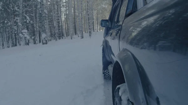 Paseos en coche en un camino forestal de invierno. Un coche en un camino cubierto de nieve entre los árboles —  Fotos de Stock