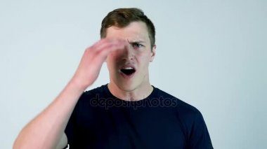 Casual giyim tutma ağız açık ve kamera beyaz arka plan karşı dururken bakarken genç adam şaşırttı. Ağır çekim