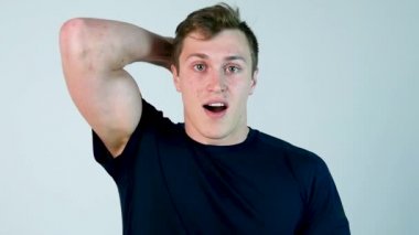 Casual giyim tutma ağız açık ve kamera beyaz arka plan karşı dururken bakarken genç adam şaşırttı. Ağır çekim