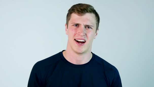 An young man yells at the camera with black t-shirt and grey background. Slow motion — Stock Video