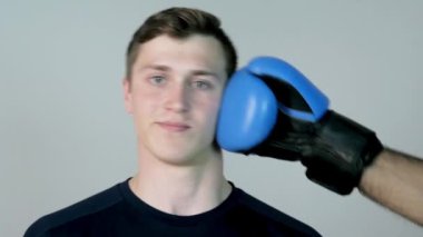 Yavaş hareket yüzüne bir yumruk çekici bir genç adam. Genç adam eldiven beyaz bir arka plan üzerinde yüzüne vurmak