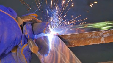 Metal kaynak kıvılcım ve duman ile. İşçi kaynak metal koruyucu maske ile. Kaynakçı metal parçalar katılır. Bir yarı otomatik kaynak kullanan işlem. Kaynak çelik. Fabrikada sanayi işçisi