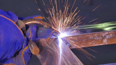 Metal kaynak kıvılcım ve duman ile. İşçi kaynak metal koruyucu maske ile. Kaynakçı metal parçalar katılır. Bir yarı otomatik kaynak kullanan işlem. Kaynak çelik. Fabrikada sanayi işçisi