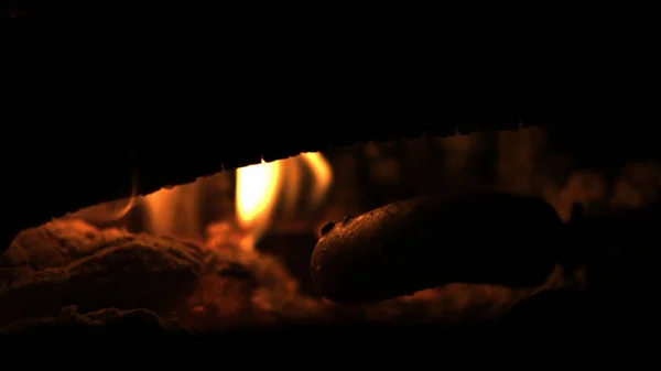 Würstchen über offenem Lagerfeuer zubereiten und zubereiten. Grillen über Lagerfeuer auf hölzernen Zweigen - Spieße in der Nacht in der Natur. — Stockfoto