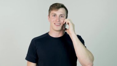 Mutlu gülümseyen genç adam beyaz arka planda cep telefonuyla konuşuyor.