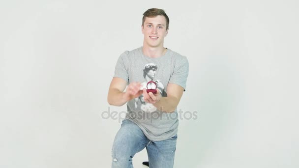 Young man makes an offer standing on his knee holding a ring on white background — Stock Video