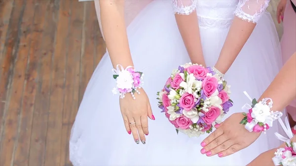 Novia y damas de honor muestran ramos de flores. La novia y sus novias se paran una al lado de la otra y muestran los ramos en sus manos. Novia con flores en la mano al aire libre. La novia está nerviosa antes de la —  Fotos de Stock