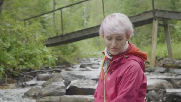 Kadın hiker ormandaki açık. Turizm kavramı. Ormandaki nehir üzerinde ceketli genç kadın — Stok video