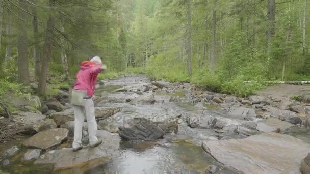 若い女性が山、岩の多い川の徒渉で旅行します。ロッキー川の上を歩く女性 — ストック動画