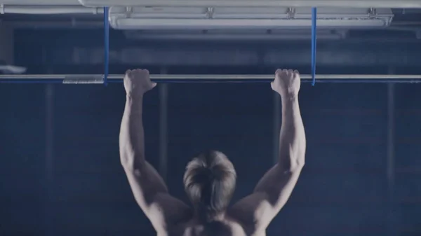 Strong man working out at a gym with bar plate. Pulls up, exercise on the shoulders and arms. Back view. Hold over head. Back view of muscular man doing pull up exercise
