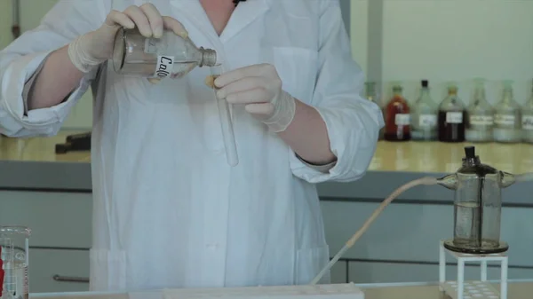Científico vertiendo químicos en un laboratorio. técnico agita matraz con reactivos. Técnico añade reactivos en el frasco — Foto de Stock