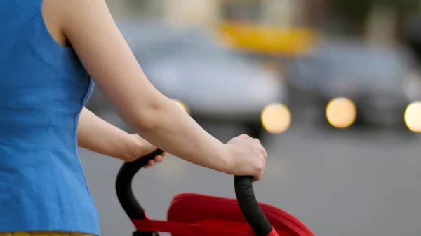 Madre joven caminando con carro de bebé en la calle vista trasera de cerca. Madre con un cochecito camina por la calle — Foto de Stock