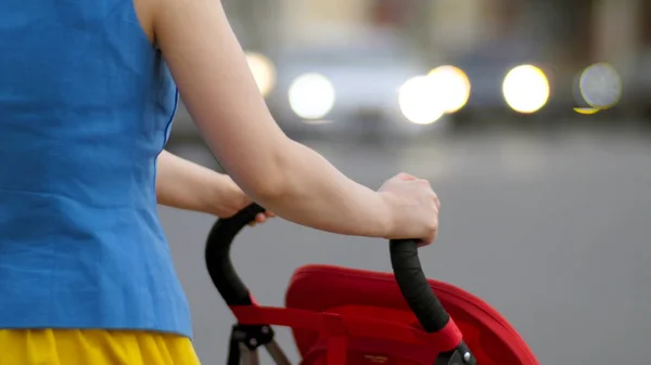 Madre joven caminando con carro de bebé en la calle vista trasera de cerca. Madre con un cochecito camina por la calle — Foto de Stock