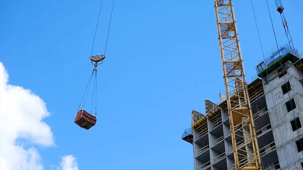 Vinç ve bina inşaat alanında mavi gökyüzü karşı. ağır yük inşaat yapım aşamasında tuğla vinç kanca asılı