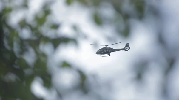 Ελικόπτερο πετώντας στον ουρανό πίσω από ή μέσω υποκαταστημάτων προβολή δέντρου. Πετούν ελικόπτερα στον ουρανό. Ελικόπτερο που φέρουν κατά το συννεφιασμένο ουρανό — Φωτογραφία Αρχείου