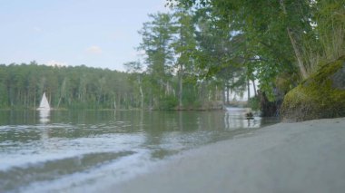 Beyaz tekne arka plan ile gölün kıyısında. Satır tekne yüzen, gökyüzü ve arka plan mükemmel yansıması ile gölde açıkta demirli. Yelkenli tekne göl kenarında