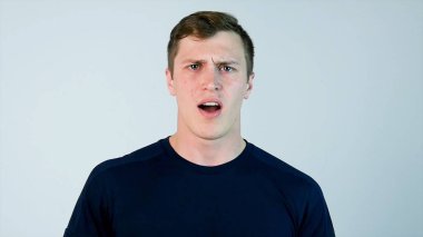 Casual giyim tutma ağız açık ve kamera beyaz arka plan karşı dururken bakarken şaşırmış genç adam