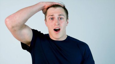 Casual giyim tutma ağız açık ve kamera beyaz arka plan karşı dururken bakarken şaşırmış genç adam
