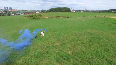 Çift havadan anket ellerde renkli duman ile alanda yürümek. Adam ve kadın üzerinde uçan renkli duman kullanarak alan üzerinden çalıştırın. Aşıklar alan üzerinden kırmızı ve pembe duman ile çalışan