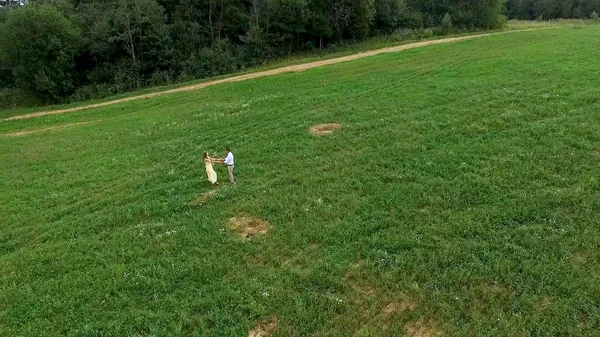 Flying over green field where the lovers walk. Aerial survey of margin where woman and man run. Field. Aerial survey of lovers run on the field