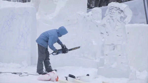 View of sculptor carving ice. Movement. Cut ice with a chainsaw. Cut and make snow sculpture. Chopping iced water with an axe. Ice Sculpture Carving. V-LOG