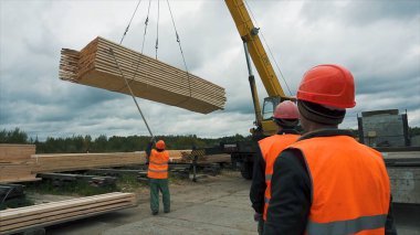 Vinç yardımıyla bir ahşap bar taşıma işçiler. Vinç yardımıyla bir ahşap bar taşıma bir inşaat işçisi. İşçiler kullanılan ahşap merdiven inşaat sahasında. Ahşap çubukların bağ.