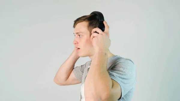 Young man puts on his headphones and listening to music on white background — Stock Photo, Image