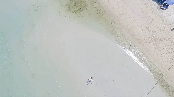 Above angle of happy wedding couple is lying on a tropical sandy beach near the ocean. Aerial view on Attractive Couple Relaxing on Sandy Beach, Tropical Vacation. Young pair lies on to the beach — Stock Photo, Image