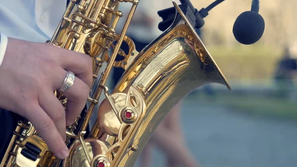 Le mani dello sposo suonano il sassofono. Mani da primo piano dell'uomo che suona il sassofono contralto dorato con effetto luce. Uomini che suonano il sassofono. Primo piano degli uomini che suonano il sassofono. contralto dorato in mani di giovane . — Foto Stock