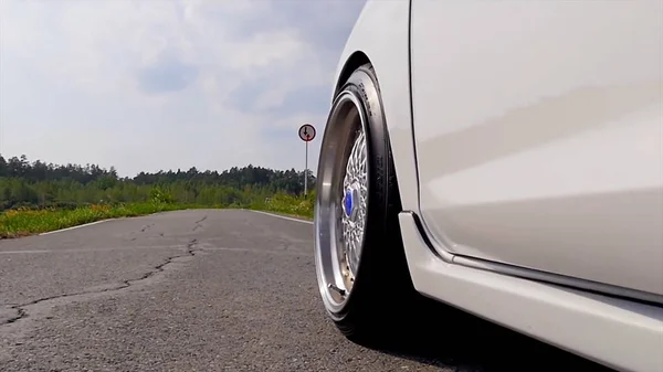 Close-up wiel sport. De scène achter als de zon naar beneden met windturbines in de rug. witte sport auto op de weg. Snelheid. Auto rijden op weg. witte sport auto in de buurt van de rivier — Stockfoto