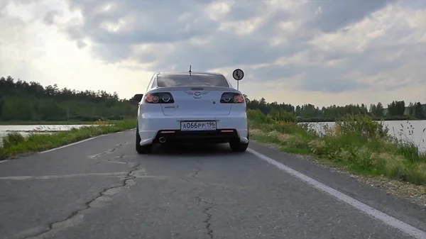 Gros plan sur le sport des roues. La scène derrière que le soleil se couche avec des éoliennes dans le dos. voiture de sport blanche sur la route. Vitesse. Voiture sur la route. voiture de sport blanche près de la rivière — Photo