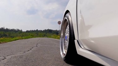 Yakın çekim tekerlek spor. Güneşin arka Rüzgar türbinleri ile aşağı gidiş olarak sahne arkasında. beyaz spor araba yolda. Hız. Yolda araba araba. beyaz spor araba Nehri yakınında