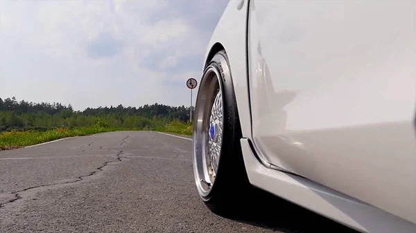 Close-up wiel sport. De scène achter als de zon naar beneden met windturbines in de rug. witte sport auto op de weg. Snelheid. Auto rijden op weg. witte sport auto in de buurt van de rivier — Stockfoto