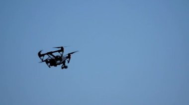 Siyah dron quadcopter üzerinde mavi gökyüzü uçan kamera ile. Siyah uçak gökyüzünde. Bağlı dijital fotoğraf makinesi için video ve fotoğraf productions ile gökyüzünde uçan quadrocopter dron