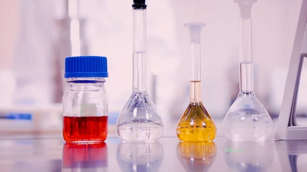 Лабораторные колбы и стаканы с жидкостями разных цветов на лабораторном столе — стоковое фото