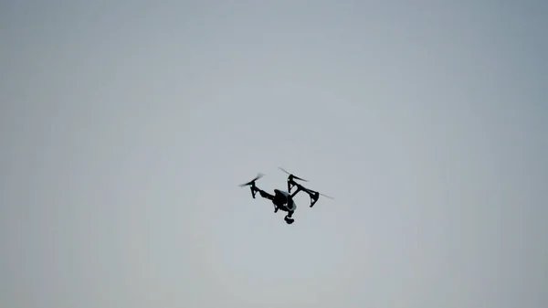 Black drone quadcopter with camera flying over blue sky. Black drone in the sky. Flying quadrocopter drone in the sky with mounted digital camera for video and photo productions — Stock Photo, Image