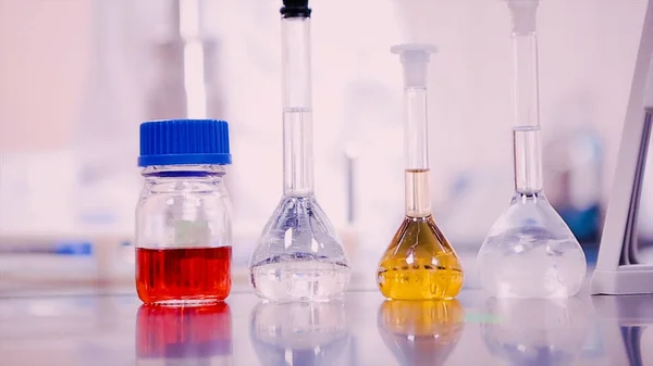 Frascos de laboratorio y vasos de precipitados con líquidos de diferentes colores en la mesa de laboratorio — Foto de Stock